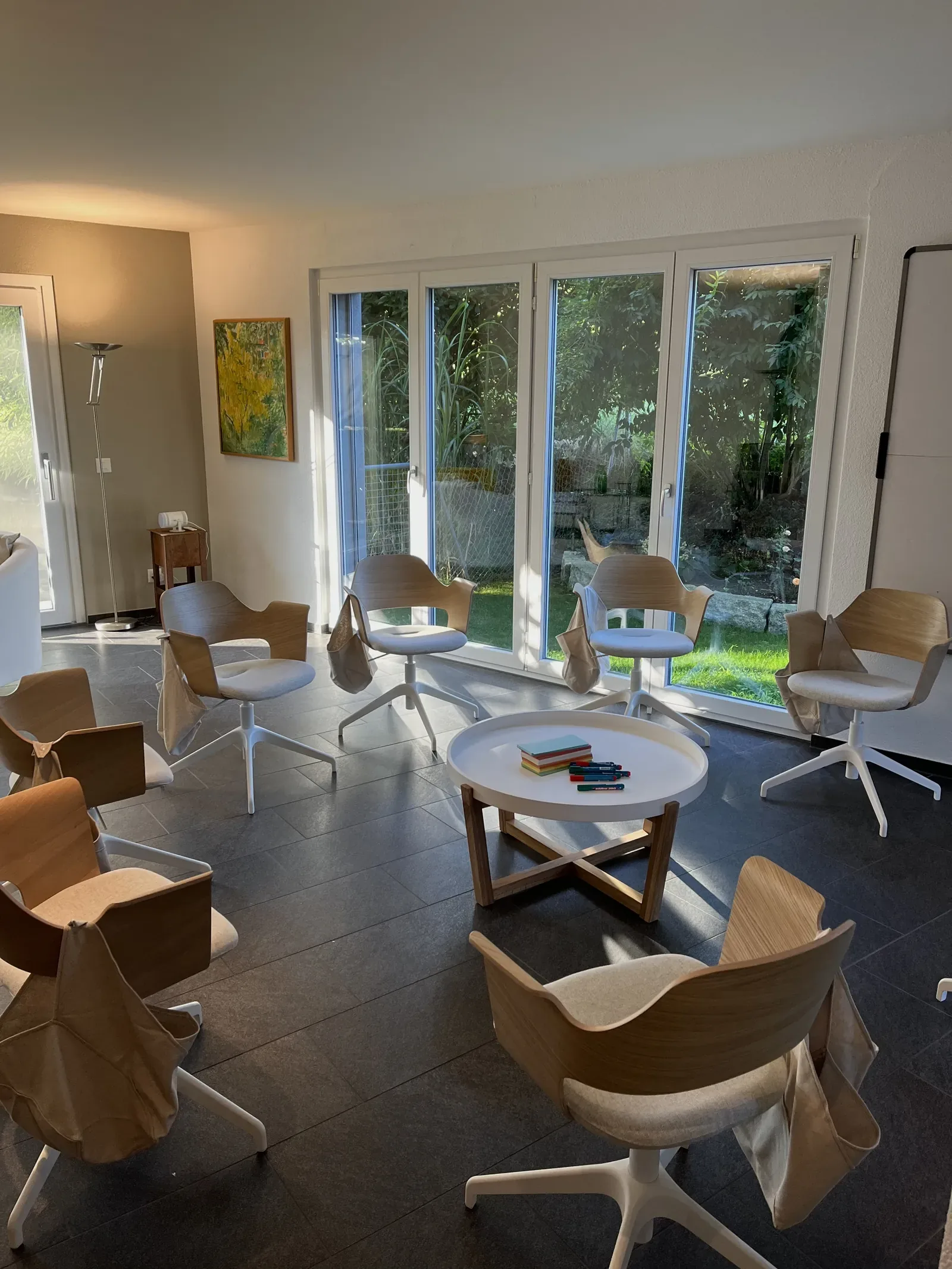 Kulturstube von Manuela Broz: Stühle im Kreis um einen kleinen Tisch mit Pinkarten, grosse Gartenfenster, ein Bild an der Wand